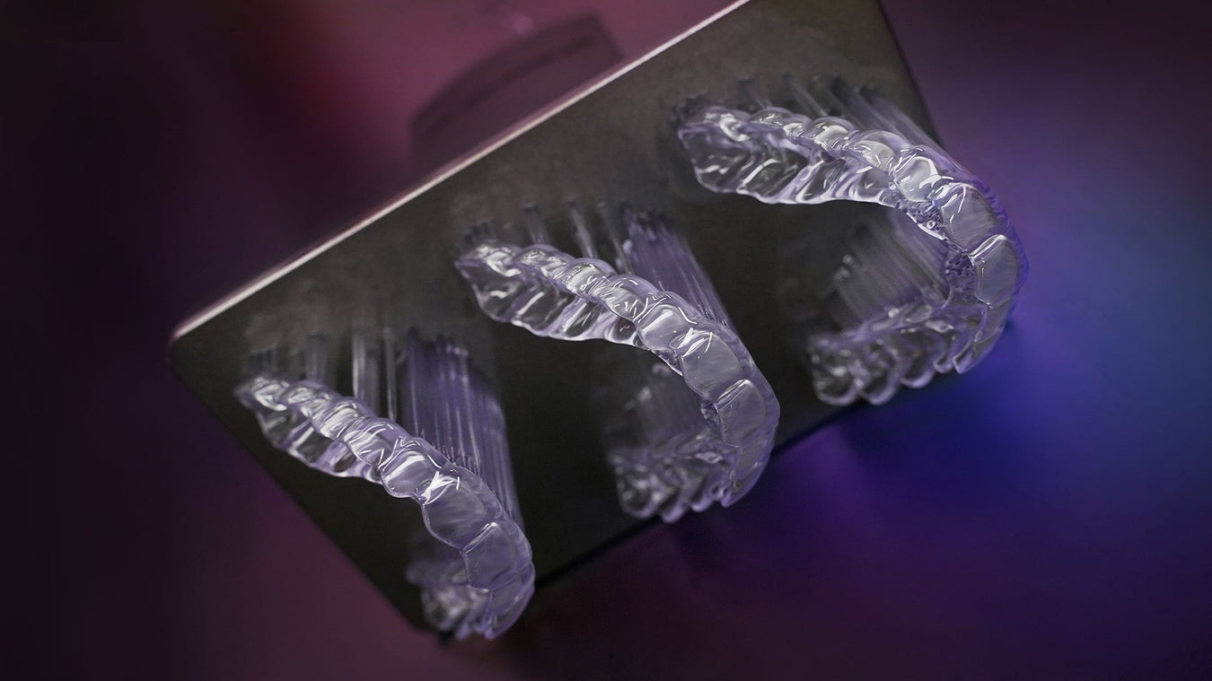 Image of a 3d printed denture base with teeth held in a hand with surgical gloves