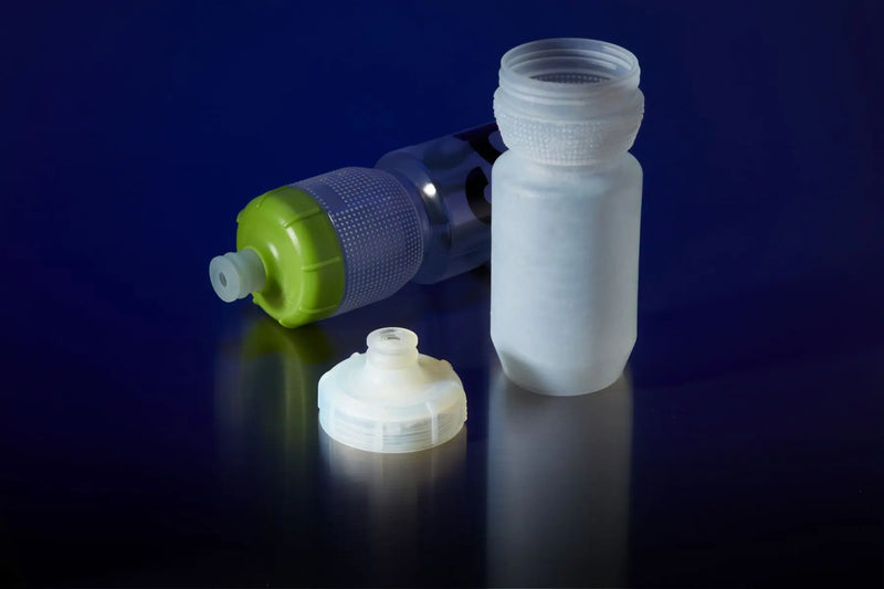 A translucent white plastic water bottle with a matching white screw cap and a separate white cap piece, shown beside a green-and-clear fitted bottle on a dark blue reflective background.
