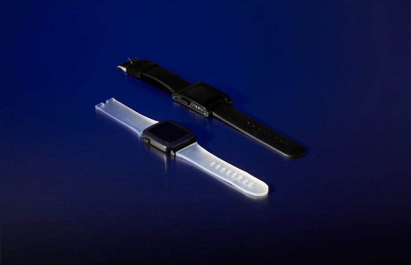 Two smartwatch bands shown on black watch faces against a dark blue gradient background. One band is matte black and the other is translucent white.
